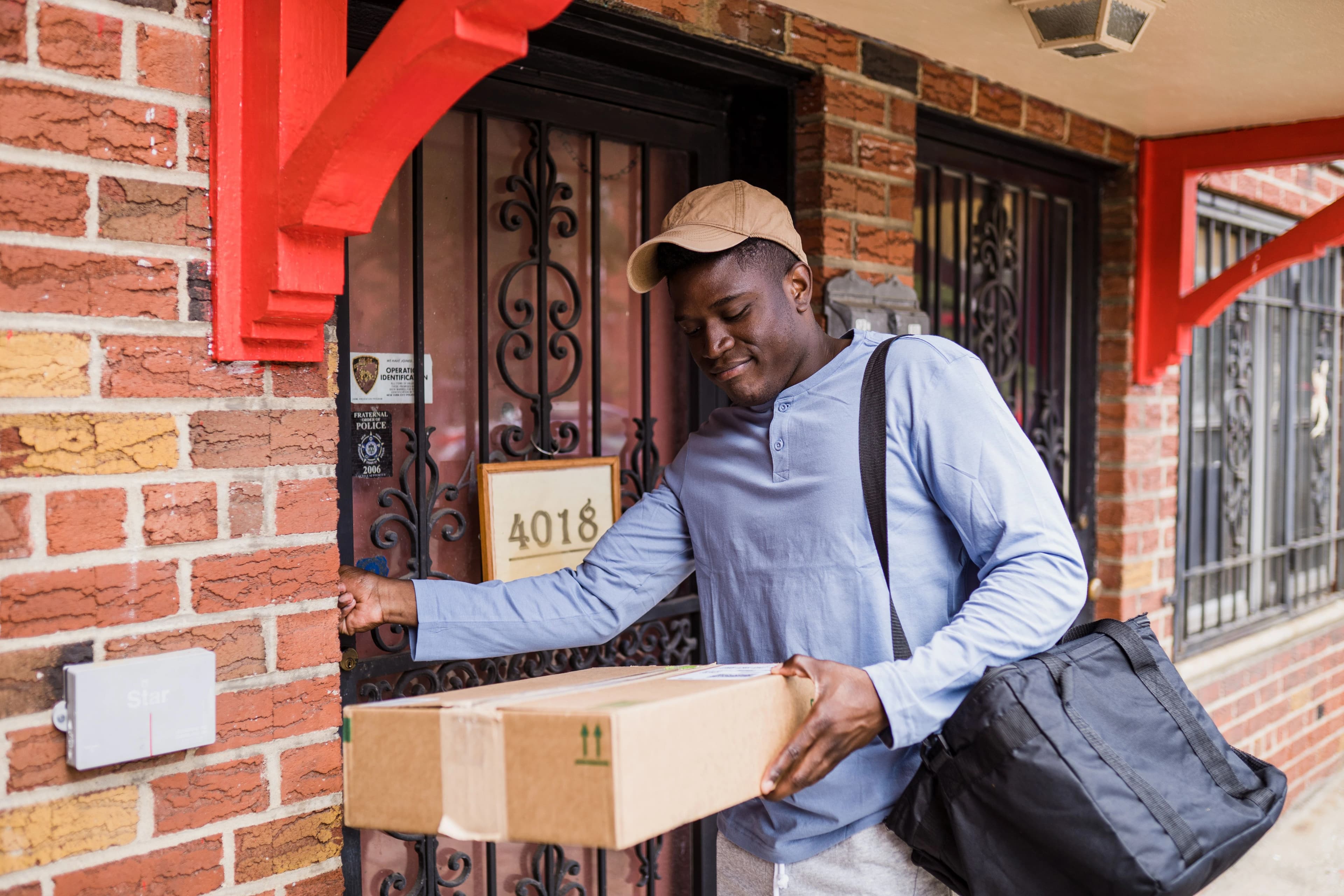 A courier carrying a parcel and a delivery bag at a customer's front door