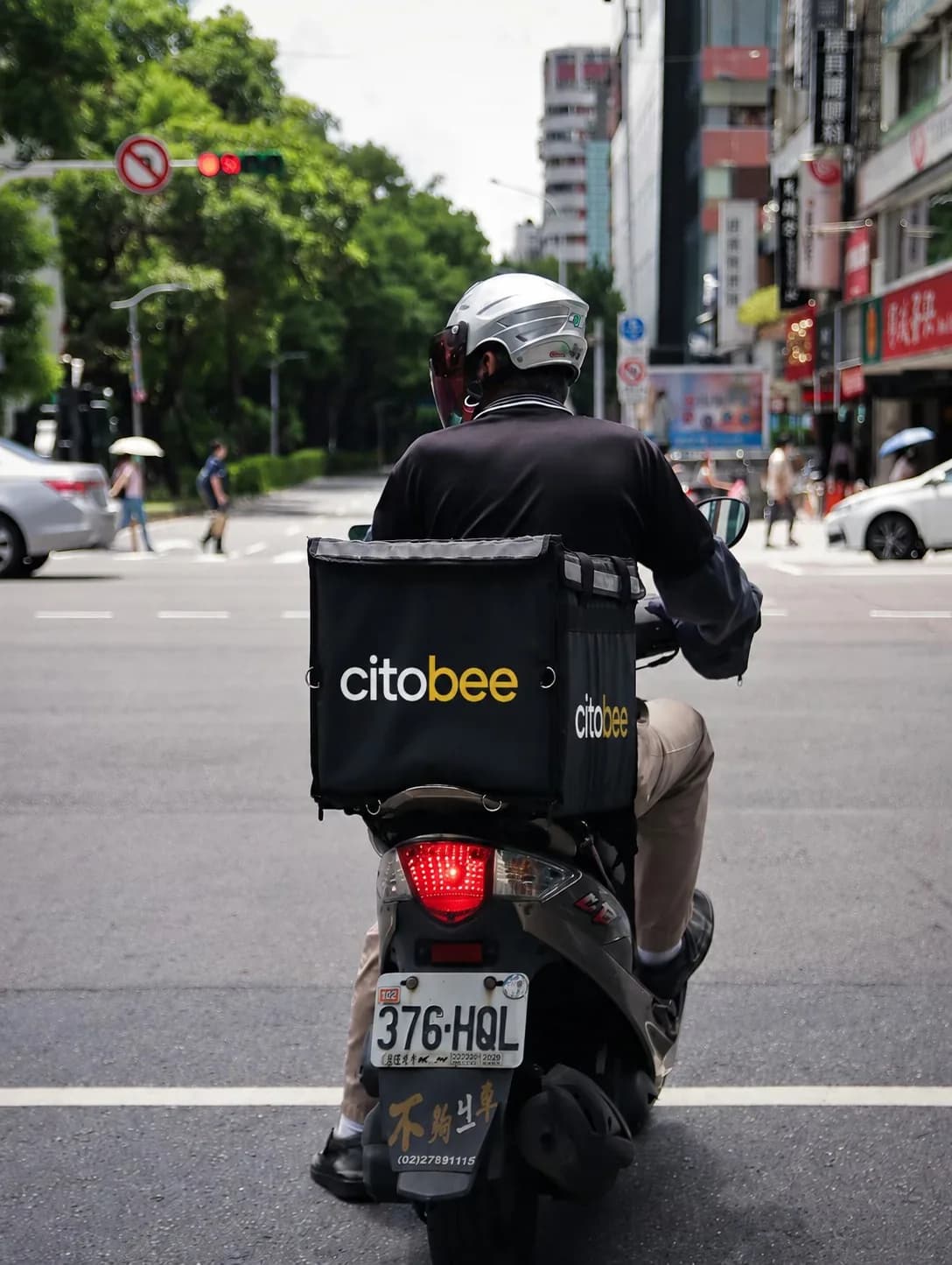 A CitoBee rider waiting at a city crossing with a branded delivery box